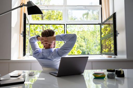 A man sitting at a desk and looking out two open windows.