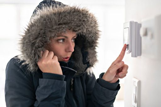 Woman adjusting thermostat in winter coat because she's cold due to the furnace not turning on.