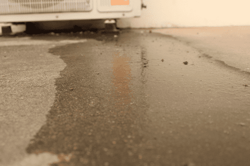 Water leaking from outdoor AC unit is spread all over the ground.