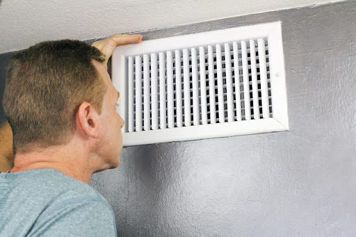 A man looking into an air vent inside a home.