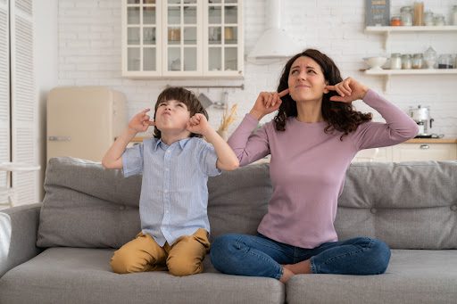 A mom and son sitting on a couch and covering their ears because of a loud sound.